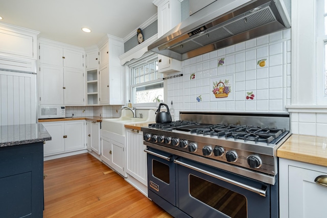 kitchen with range with two ovens, decorative backsplash, light wood-style floors, exhaust hood, and white cabinetry