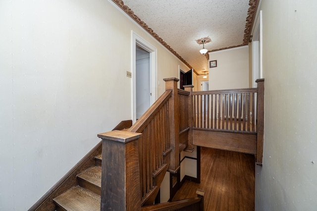 stairs with a textured ceiling, crown molding, baseboards, and wood finished floors