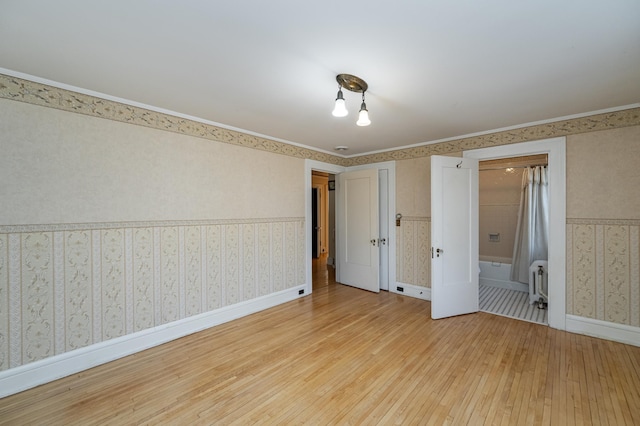 empty room with wallpapered walls, radiator heating unit, baseboards, and light wood-type flooring