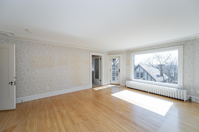 spare room featuring wallpapered walls, radiator heating unit, wood finished floors, and a wealth of natural light