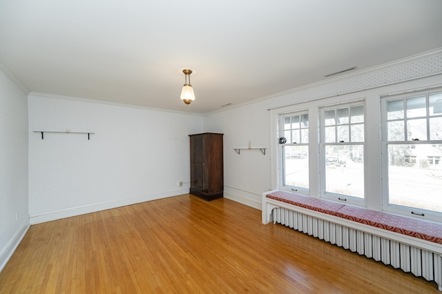 spare room with light wood-style flooring, radiator, a wealth of natural light, and ornamental molding