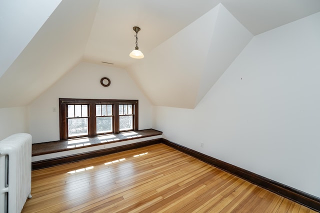 bonus room featuring baseboards, light wood-type flooring, radiator heating unit, and lofted ceiling