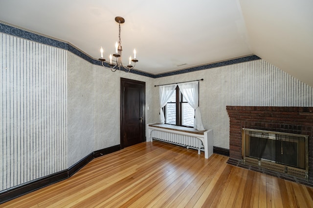 unfurnished living room with wallpapered walls, vaulted ceiling, radiator, and wood-type flooring