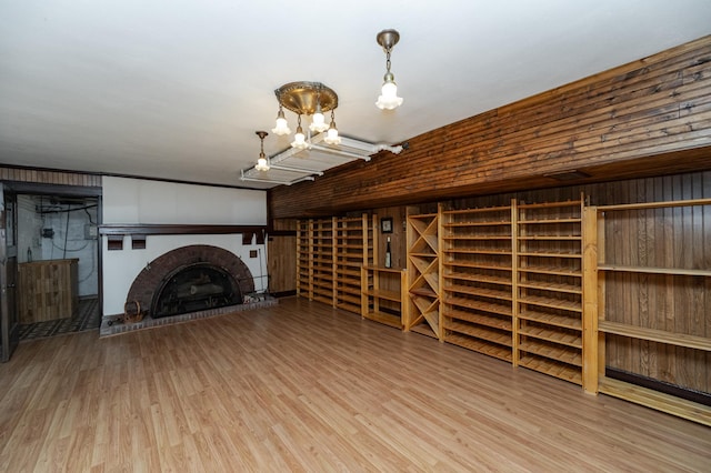 unfurnished living room with a notable chandelier, a brick fireplace, and wood finished floors