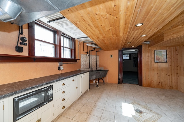 kitchen featuring wooden walls, black microwave, light tile patterned floors, wooden ceiling, and white cabinets