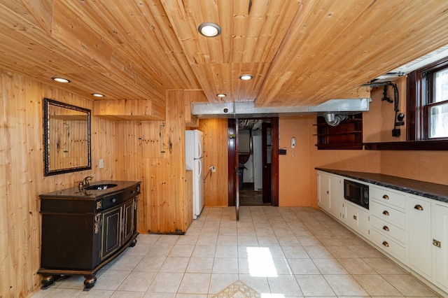 kitchen with freestanding refrigerator, a sink, black microwave, white cabinetry, and dark countertops