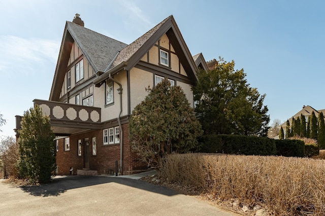 view of home's exterior featuring brick siding, stucco siding, a chimney, and a shingled roof