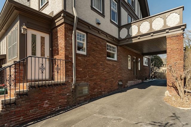 view of side of home with driveway, stucco siding, a carport, crawl space, and brick siding