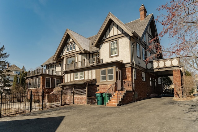 view of front of property featuring brick siding, fence, stucco siding, a chimney, and a balcony