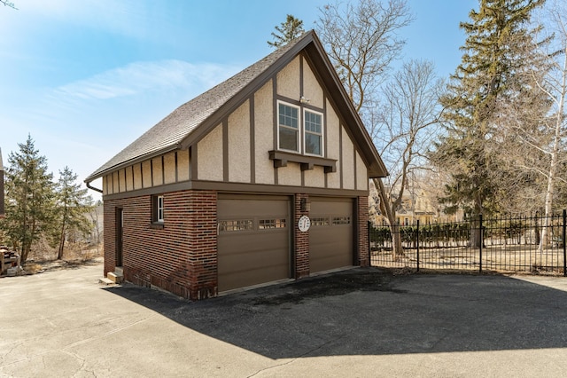 view of property exterior featuring stucco siding, driveway, fence, a garage, and brick siding