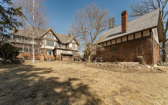 back of property featuring a balcony, brick siding, and a chimney