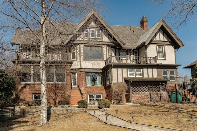 rear view of property featuring stucco siding, a balcony, fence, brick siding, and a chimney