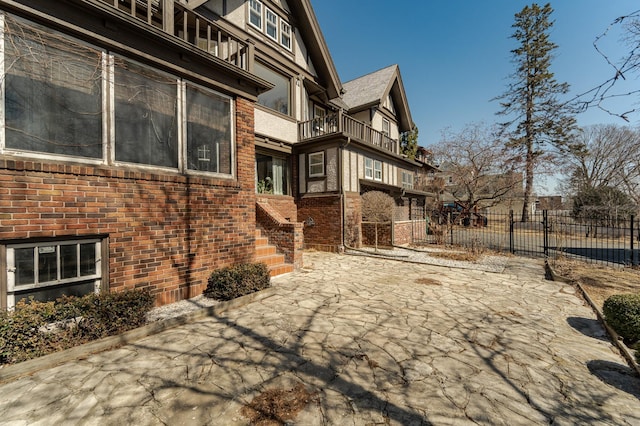 view of side of property with brick siding, a balcony, and fence