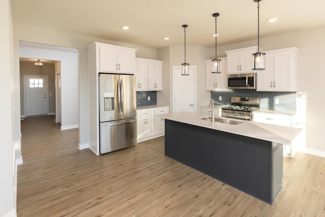 kitchen featuring stainless steel appliances, decorative light fixtures, a center island with sink, white cabinets, and light wood-type flooring