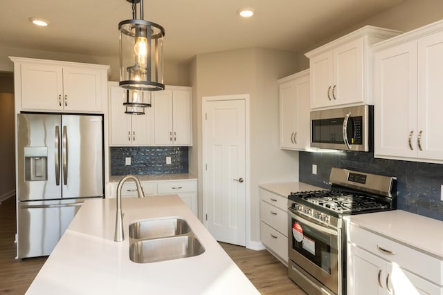 kitchen featuring sink, hanging light fixtures, stainless steel appliances, hardwood / wood-style floors, and white cabinets