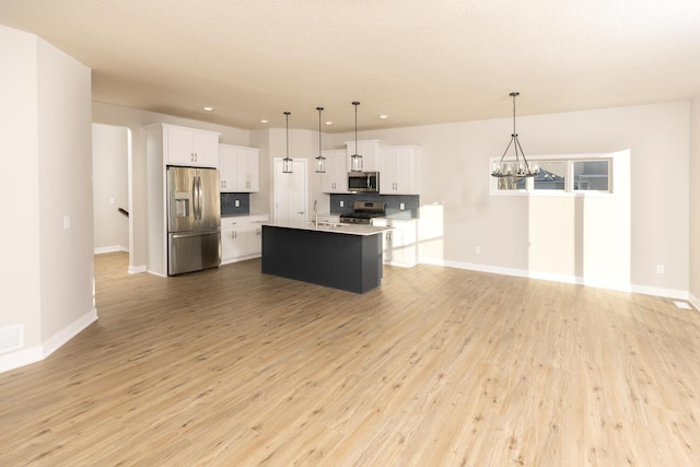 kitchen featuring appliances with stainless steel finishes, light wood-type flooring, a kitchen island with sink, white cabinetry, and hanging light fixtures