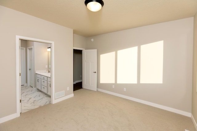 unfurnished bedroom with a textured ceiling, light colored carpet, ensuite bath, and sink