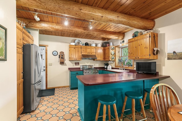 kitchen with under cabinet range hood, dark countertops, freestanding refrigerator, a peninsula, and range