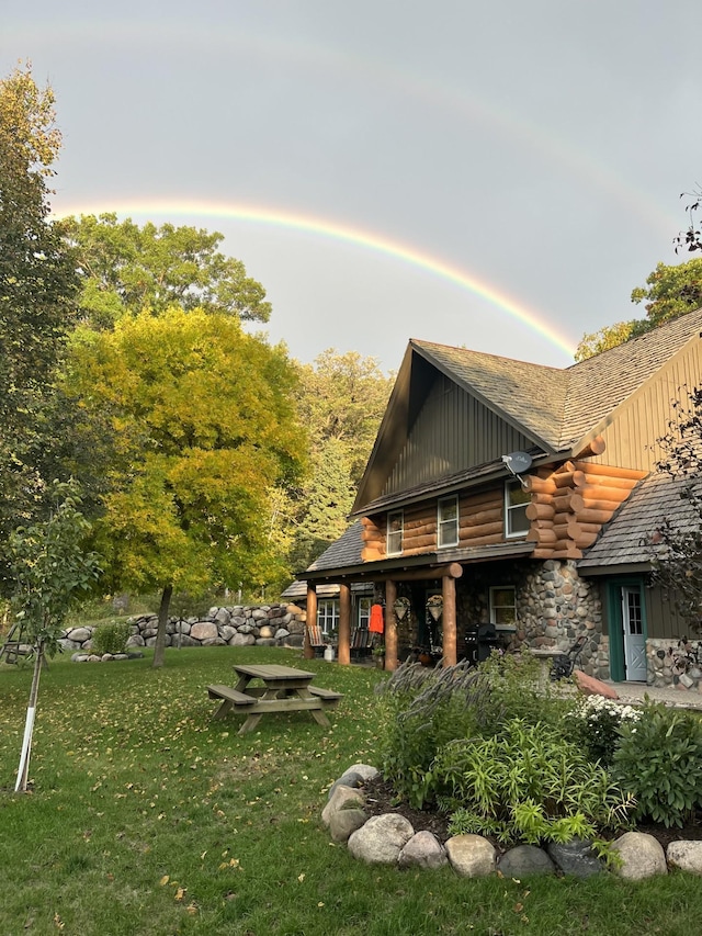 back of house at dusk featuring a yard, stone siding, and board and batten siding