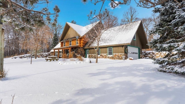 view of snowy exterior with log siding, a garage, and stone siding