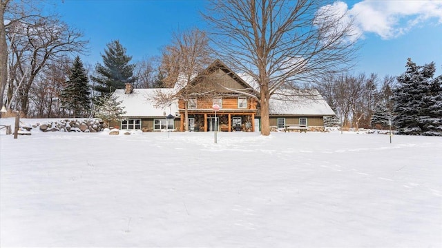 snow covered rear of property with a chimney and a sunroom