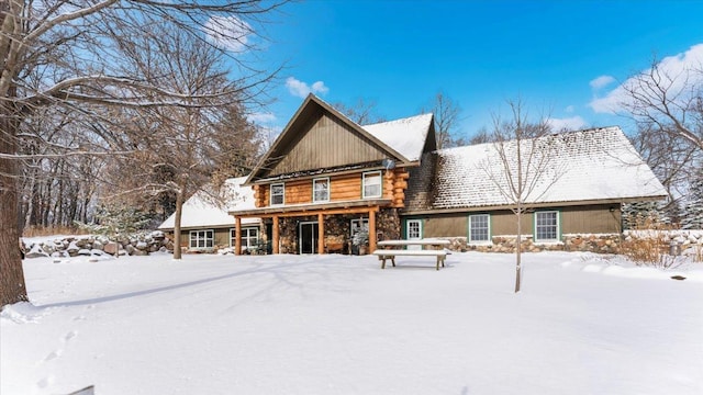 snow covered back of property with stone siding