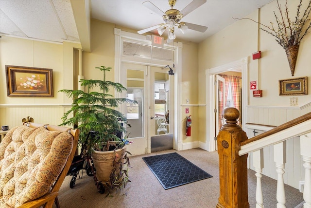 entrance foyer with carpet flooring, ceiling fan, and wooden walls