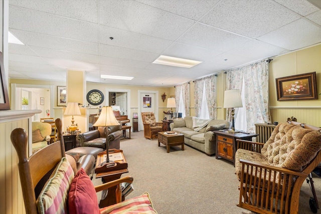 living room with a paneled ceiling, light carpet, and wood walls