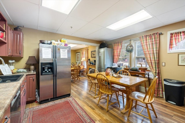 dining room with a drop ceiling, sink, and light hardwood / wood-style flooring