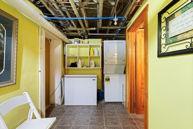 clothes washing area featuring dark tile patterned flooring and stacked washer and clothes dryer