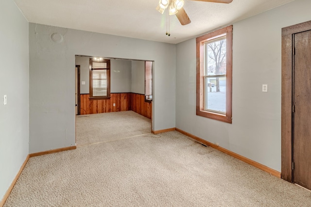 carpeted empty room with ceiling fan, a textured ceiling, and wooden walls