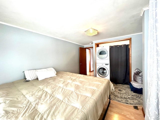 bedroom featuring crown molding, hardwood / wood-style floors, and stacked washing maching and dryer