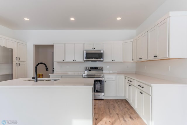 kitchen with appliances with stainless steel finishes, a kitchen island with sink, sink, light hardwood / wood-style flooring, and white cabinets