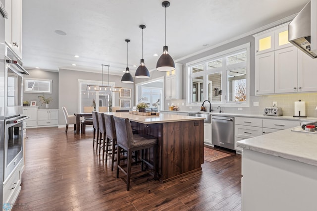 kitchen with pendant lighting, white cabinets, appliances with stainless steel finishes, a kitchen island, and dark hardwood / wood-style flooring