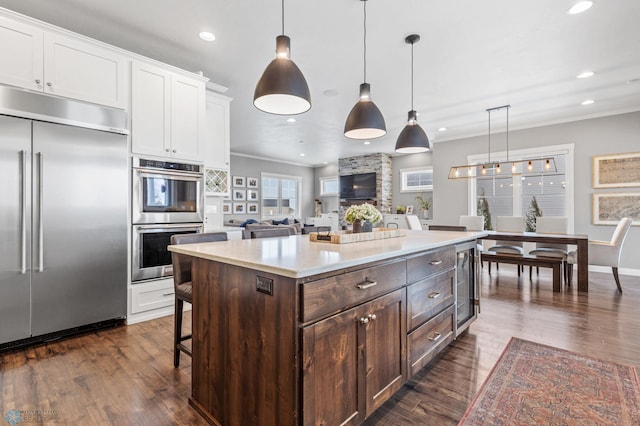 kitchen with dark wood-type flooring, stainless steel appliances, decorative light fixtures, dark brown cabinets, and white cabinets