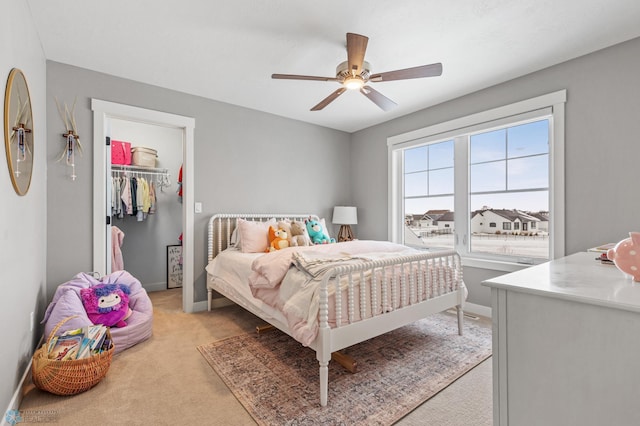 bedroom with a walk in closet, ceiling fan, a closet, and light colored carpet