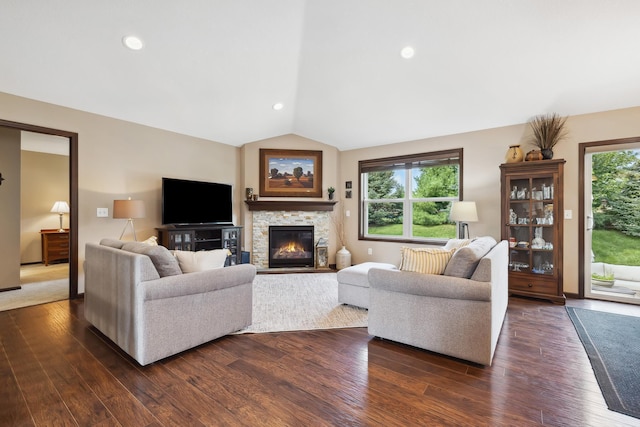 living room featuring lofted ceiling, a healthy amount of sunlight, a stone fireplace, and dark hardwood / wood-style floors