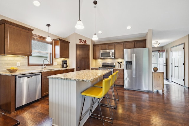 kitchen featuring pendant lighting, sink, appliances with stainless steel finishes, a center island, and light stone countertops