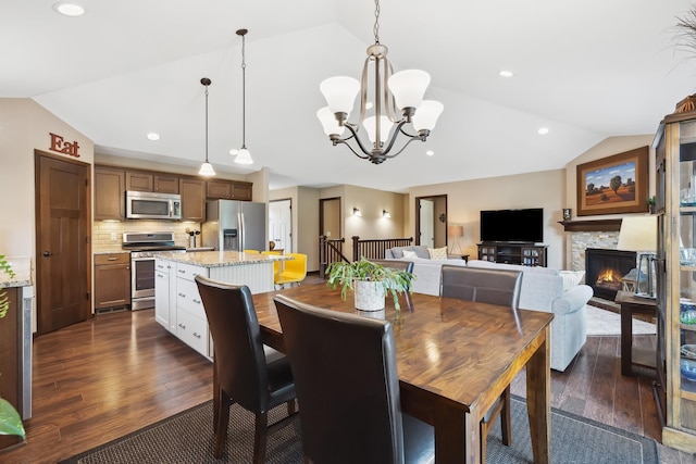 dining area with dark wood-type flooring, lofted ceiling, a fireplace, and a notable chandelier