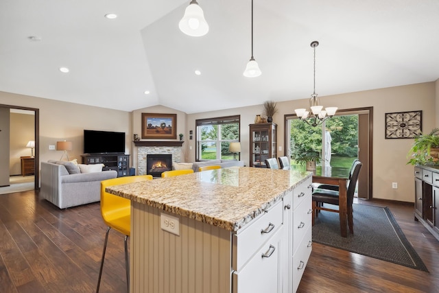 kitchen with lofted ceiling, white cabinetry, a kitchen breakfast bar, a center island, and light stone countertops