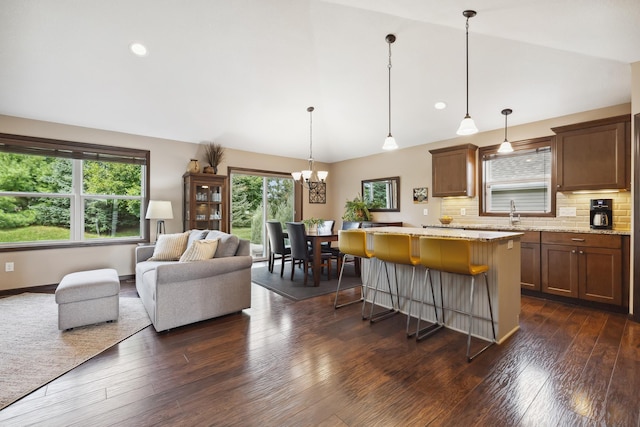 kitchen featuring pendant lighting, vaulted ceiling, light stone countertops, and a kitchen bar