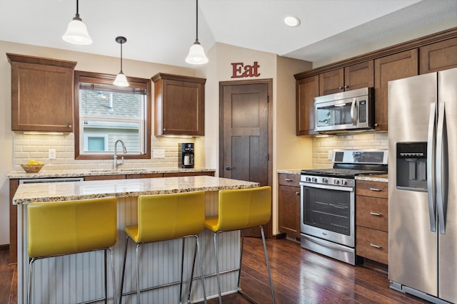 kitchen with a center island, appliances with stainless steel finishes, light stone countertops, and hanging light fixtures