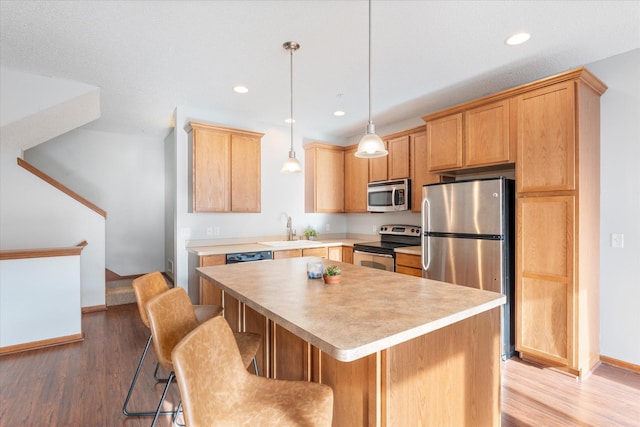 kitchen with sink, light hardwood / wood-style flooring, a kitchen island, and appliances with stainless steel finishes