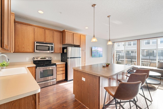 kitchen with sink, stainless steel appliances, light hardwood / wood-style flooring, decorative light fixtures, and a kitchen island