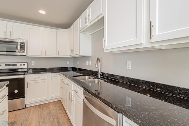 kitchen with sink, light hardwood / wood-style flooring, dark stone counters, white cabinets, and appliances with stainless steel finishes