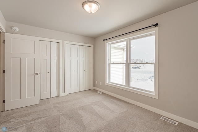 unfurnished bedroom with light colored carpet and two closets