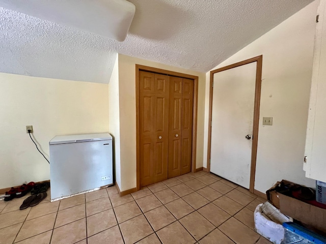 interior space featuring a textured ceiling, lofted ceiling, fridge, a closet, and light tile patterned flooring