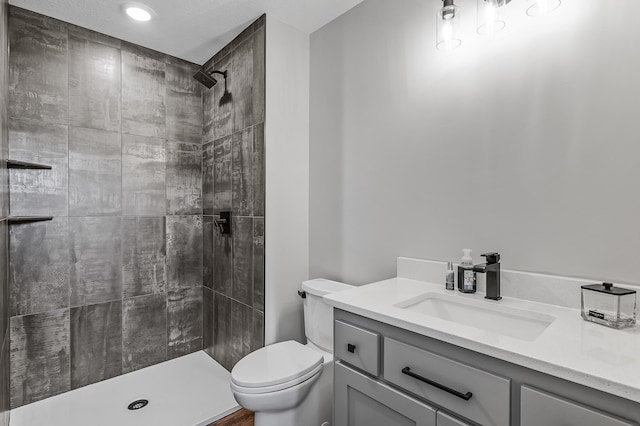 bathroom with a tile shower, vanity, and toilet