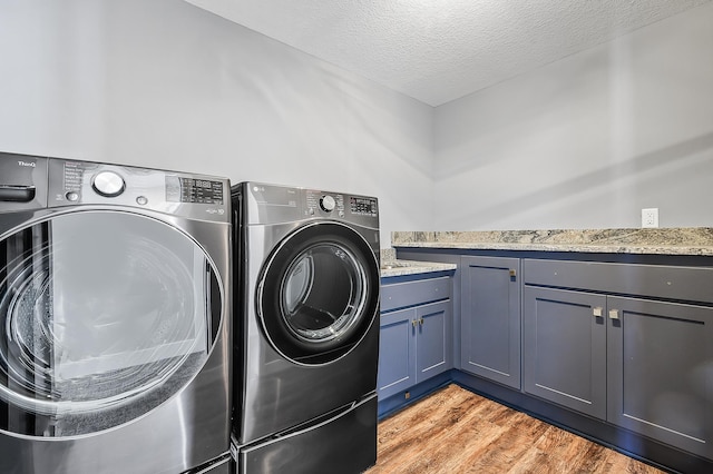 laundry area featuring washer and dryer, light hardwood / wood-style floors, cabinets, and a textured ceiling