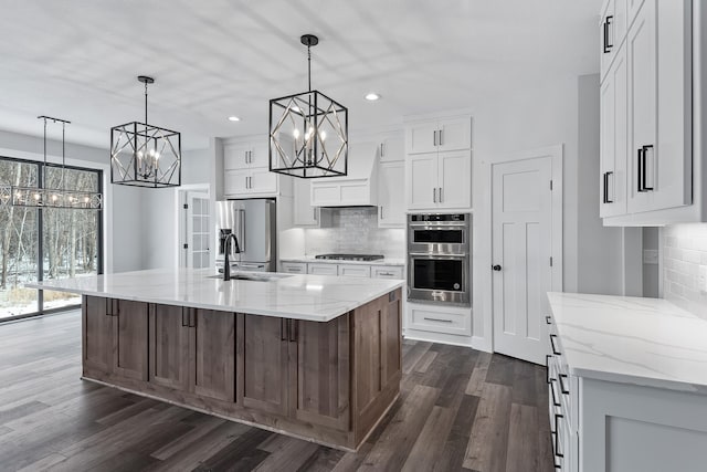 kitchen featuring a large island with sink, white cabinets, sink, dark hardwood / wood-style floors, and appliances with stainless steel finishes